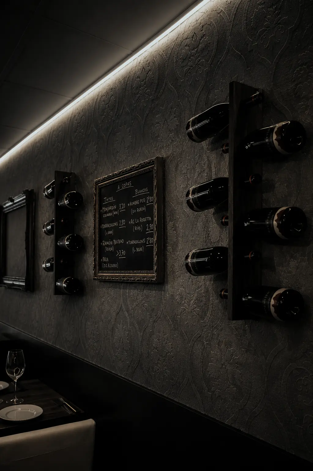 La paret del celler del Síbaris: botellers de fusta, la pissarra de vins i la llum lineal càlida